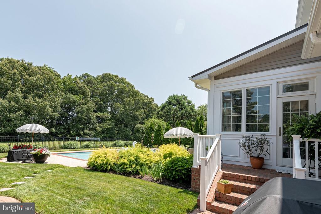 White home’s backyard with brick steps, landscaped lawn, patio seating, and a swimming pool.