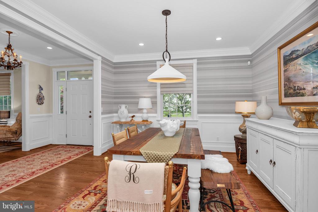 Dining room with a long wooden table, striped wallpaper, and white wainscoting.