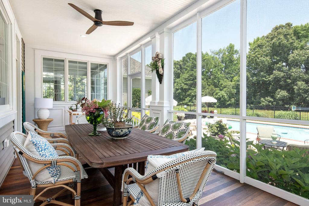 Furnished sunroom with a wood dining table and large windows overlooking a swimming pool.