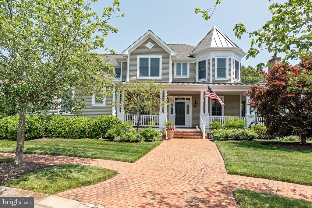 Gray two-story home with a wraparound porch, turret, and curved brick walkway.