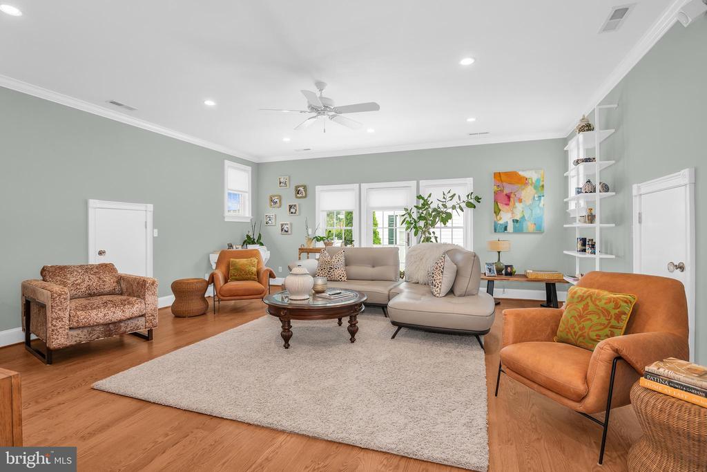 Living room with a gray sectional, orange accent chairs, sage-green walls, and warm wood floors.