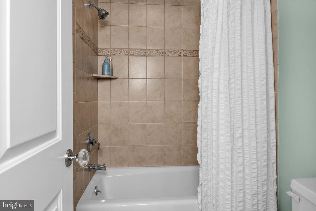 Bathroom with a white bathtub and beige tiled shower surround behind a white curtain.