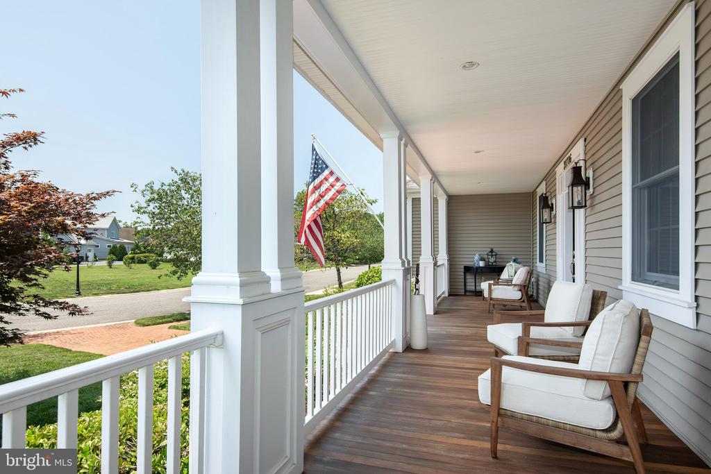 Covered home porch with white columns, cushioned chairs, and an American flag overlooking the lawn.
