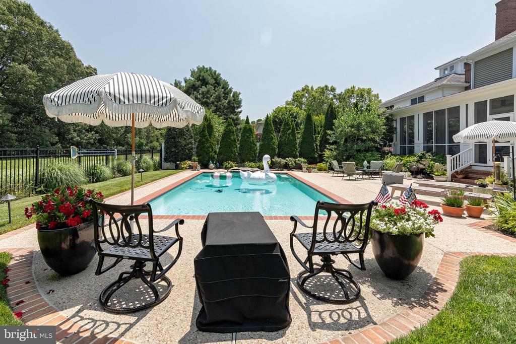 Backyard swimming pool with striped umbrellas, patio seating, and flower planters beside a screened porch.