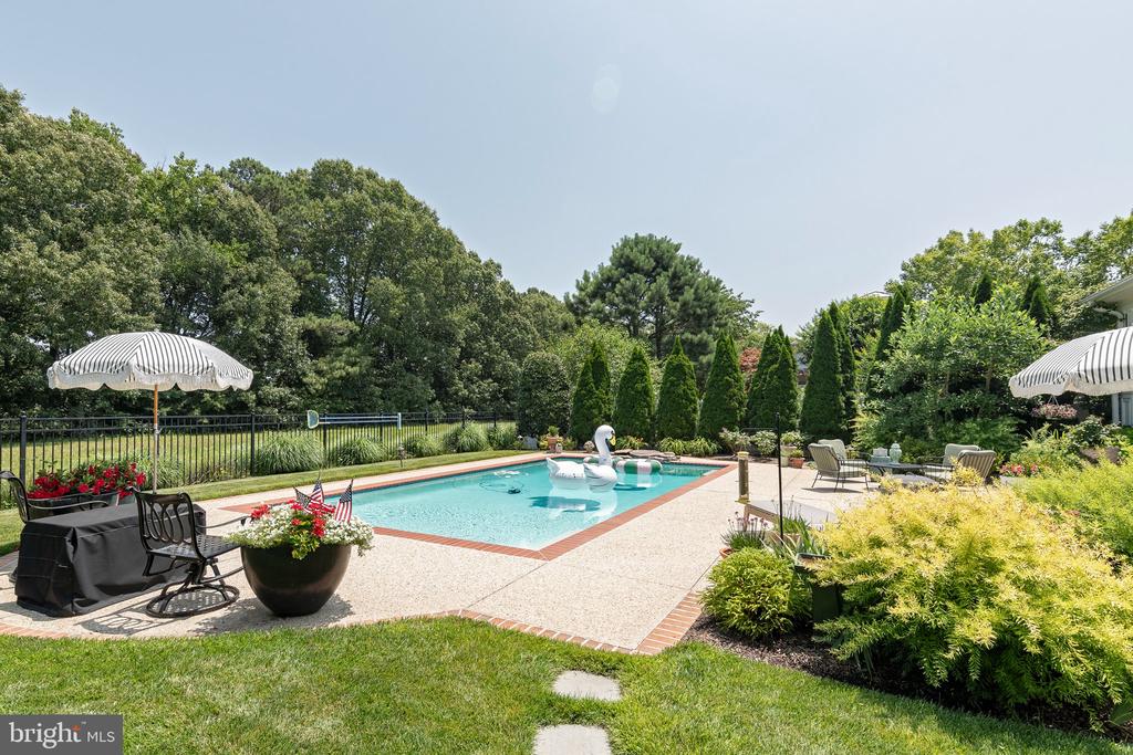 Backyard swimming pool with a swan float, striped umbrellas, patio seating, and landscaped garden.
