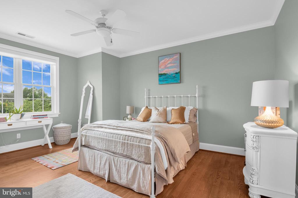 Bedroom with a white metal bed, sage-gray walls, hardwood floors, and a large window overlooking trees.