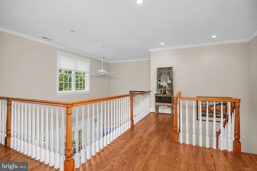 Upstairs landing with hardwood floors, wood-and-white railings, a window, and a ceiling fan.