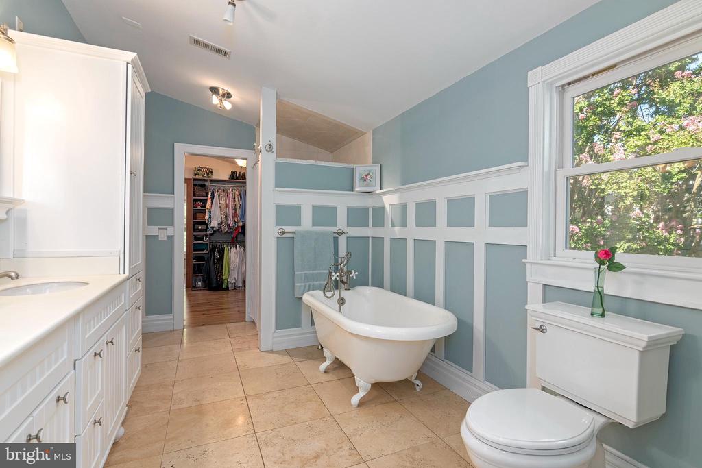 Bathroom with a freestanding clawfoot tub, blue walls, white paneling, and a large window.