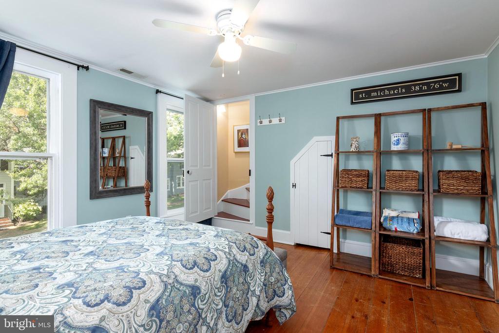 Bedroom with pale blue walls, patterned bedspread, and wooden shelving with baskets.