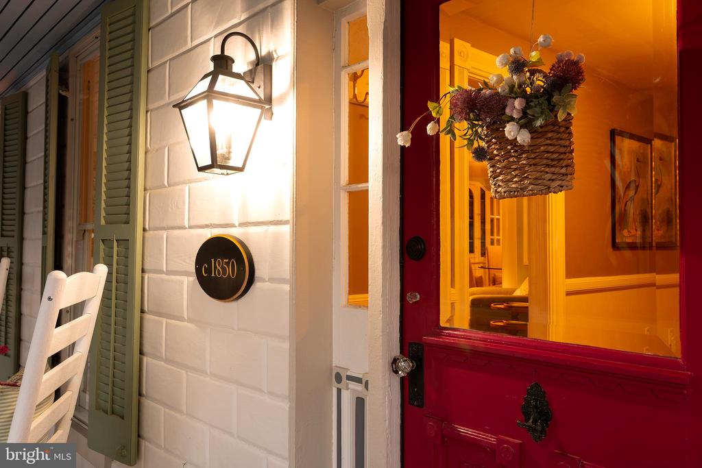 Historic home entrance with a red front door, glowing lantern, and “c 1850” plaque.