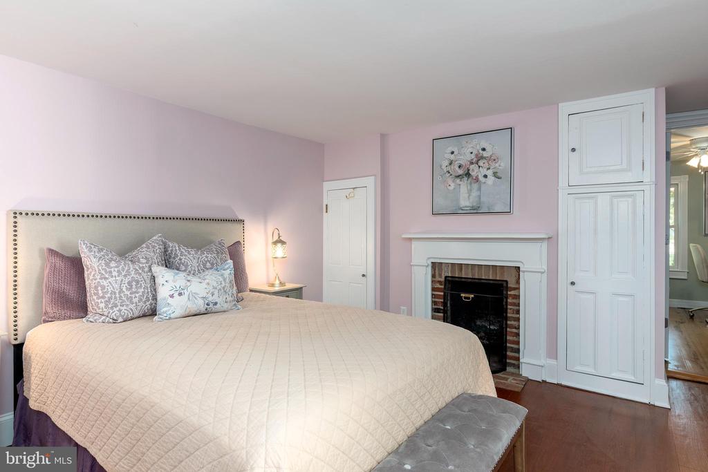 Bedroom with a large bed and a white-trimmed brick fireplace against pale pink walls.