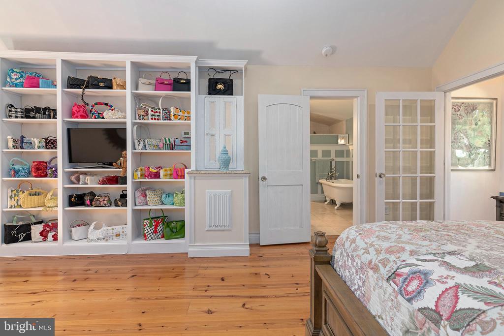 Bedroom with built-in display shelves, hardwood flooring, and an open doorway to a bathroom.