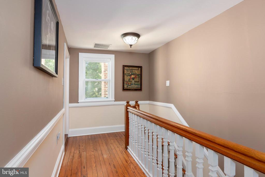 Upstairs landing with hardwood floors, a wood-and-white staircase railing, and a bright window.