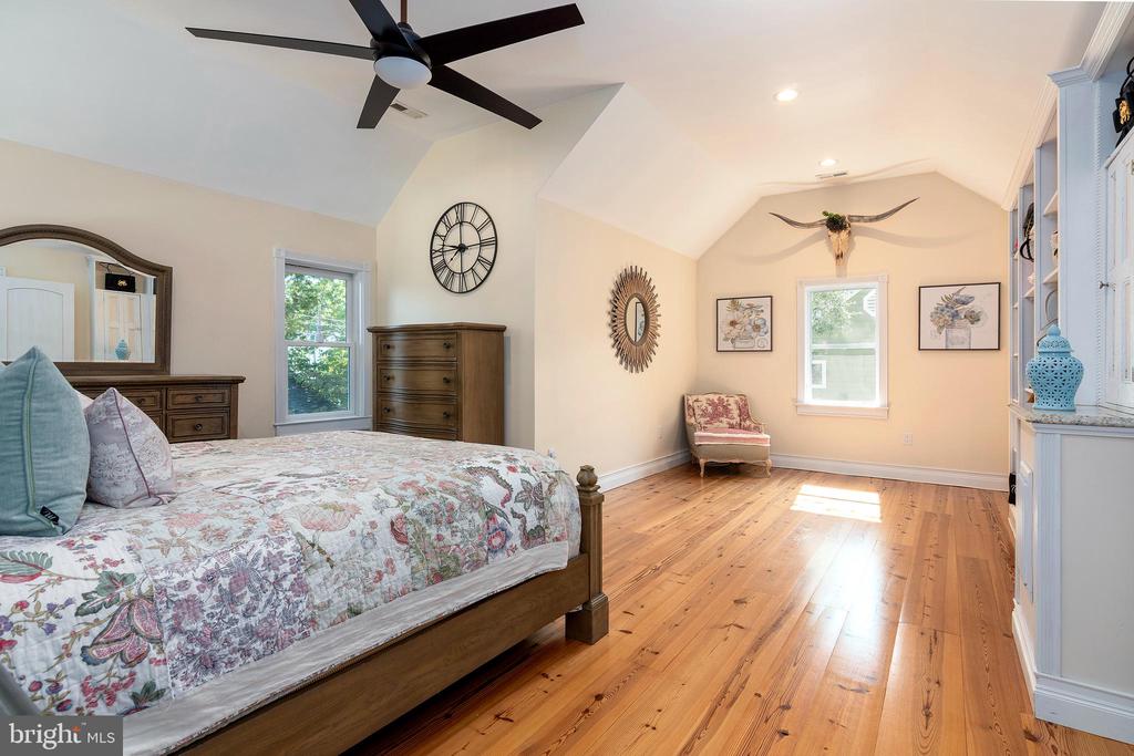 Bedroom with a floral quilt, warm hardwood floors, and a bright window-side sitting area.