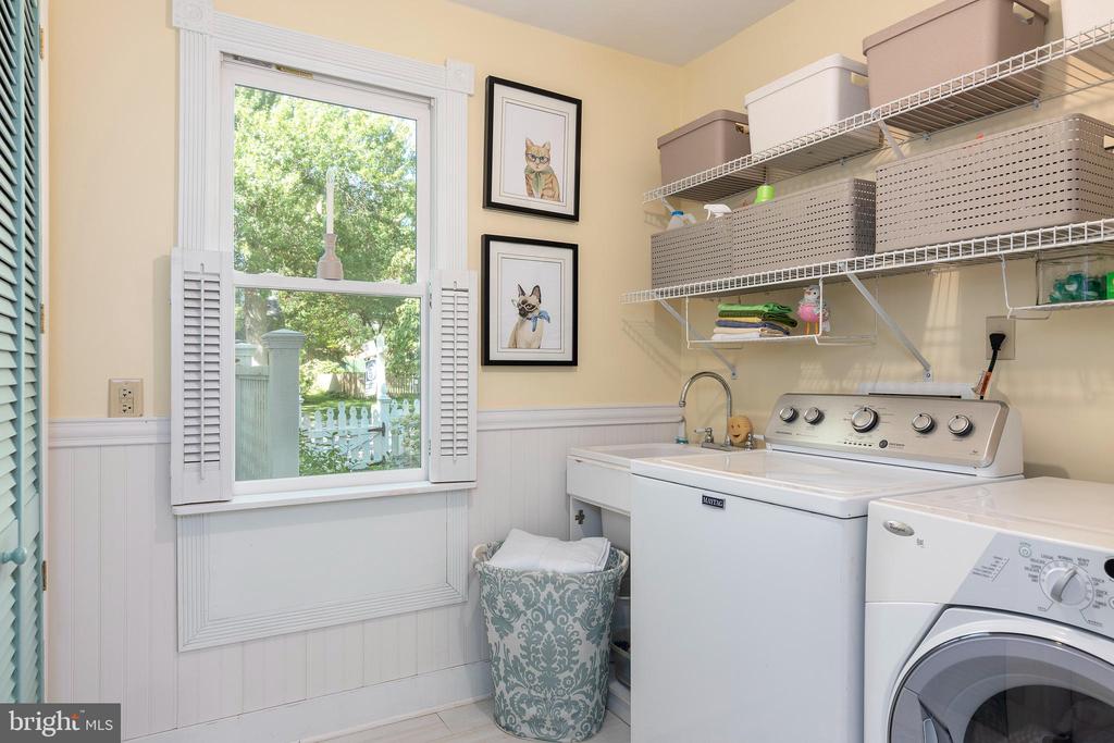 Laundry room with two washers, a utility sink, and open storage shelves beside a shuttered window.