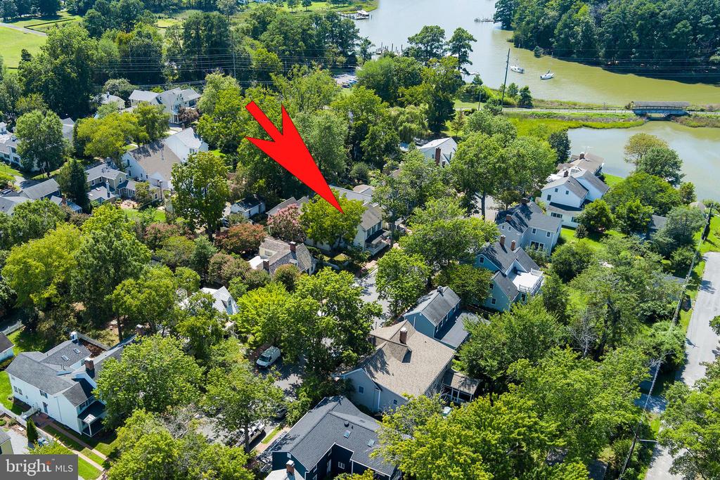 Aerial view of the red-arrow-marked home among leafy homes near the water.