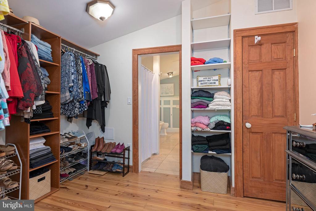 Walk-in closet with open clothing shelves, neatly arranged shoes, and a doorway to a tiled bathroom.