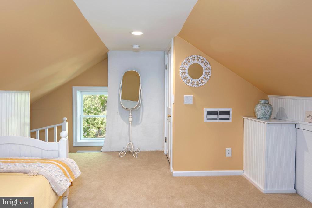 Attic bedroom with sloped yellow ceilings, a white bed, and a freestanding mirror.