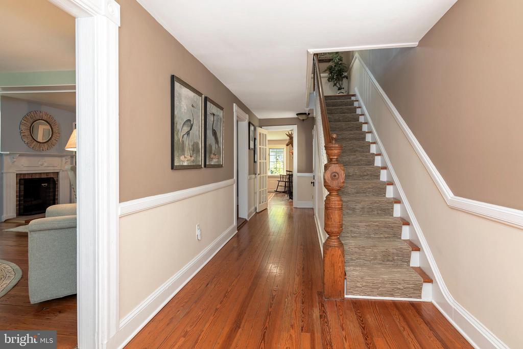 Hallway with polished hardwood floors and a carpeted staircase beside a sitting room fireplace.