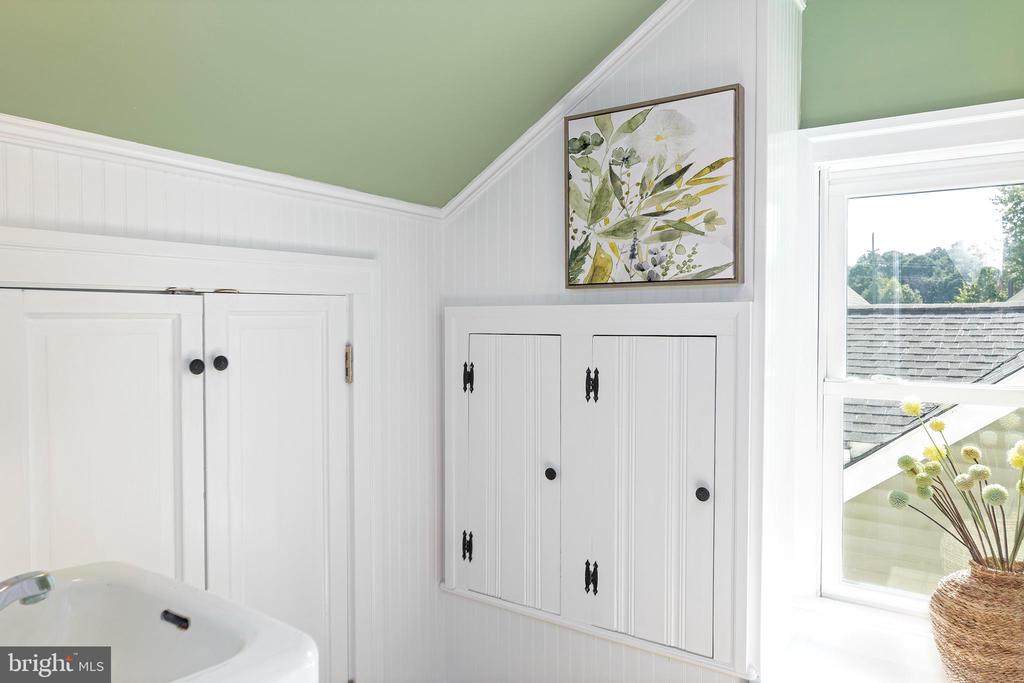 Bathroom with white beadboard walls, built-in cabinets, green ceiling, and framed botanical artwork.