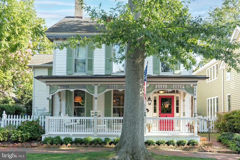 Two-story house with a broad porch, green shutters, and a red front door, partly obscured by a large tree.