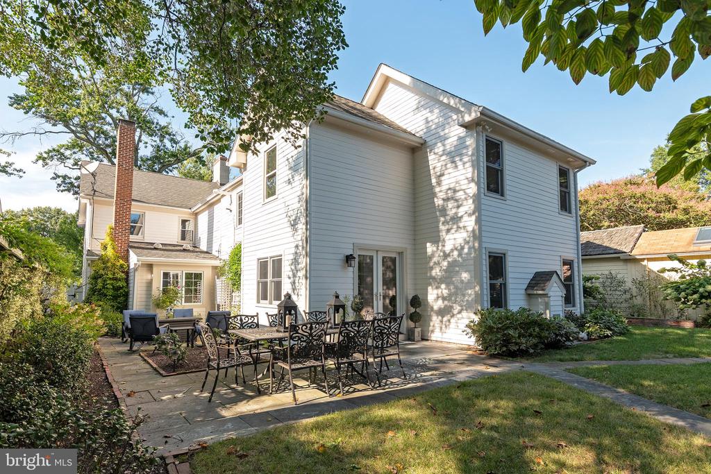 Two-story house with a furnished stone patio, French doors, and a lawn.