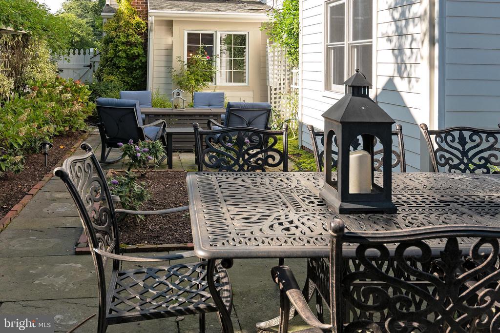 Paved courtyard patio with ornate metal furniture, a lantern, and garden beds beside the house.