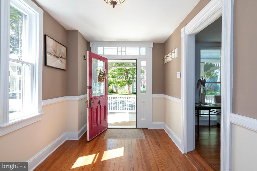 Entry hall with hardwood floors and an open red front door overlooking a porch and garden.