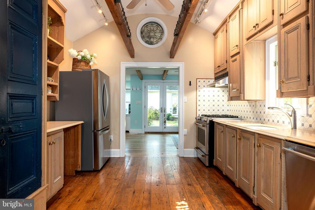 Galley kitchen with warm wood cabinets, exposed beams, hardwood floors, and a stainless steel refrigerator.