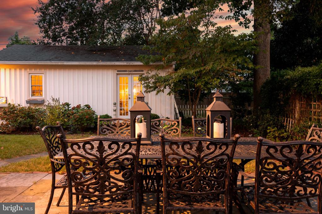 Backyard patio with ornate metal dining set and two lit outdoor fireplaces at dusk.