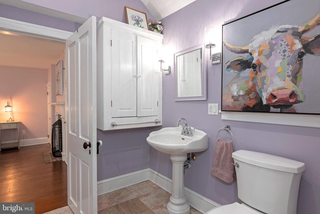 Bathroom with lavender walls, a pedestal sink, white cabinetry, and a colorful cow painting.