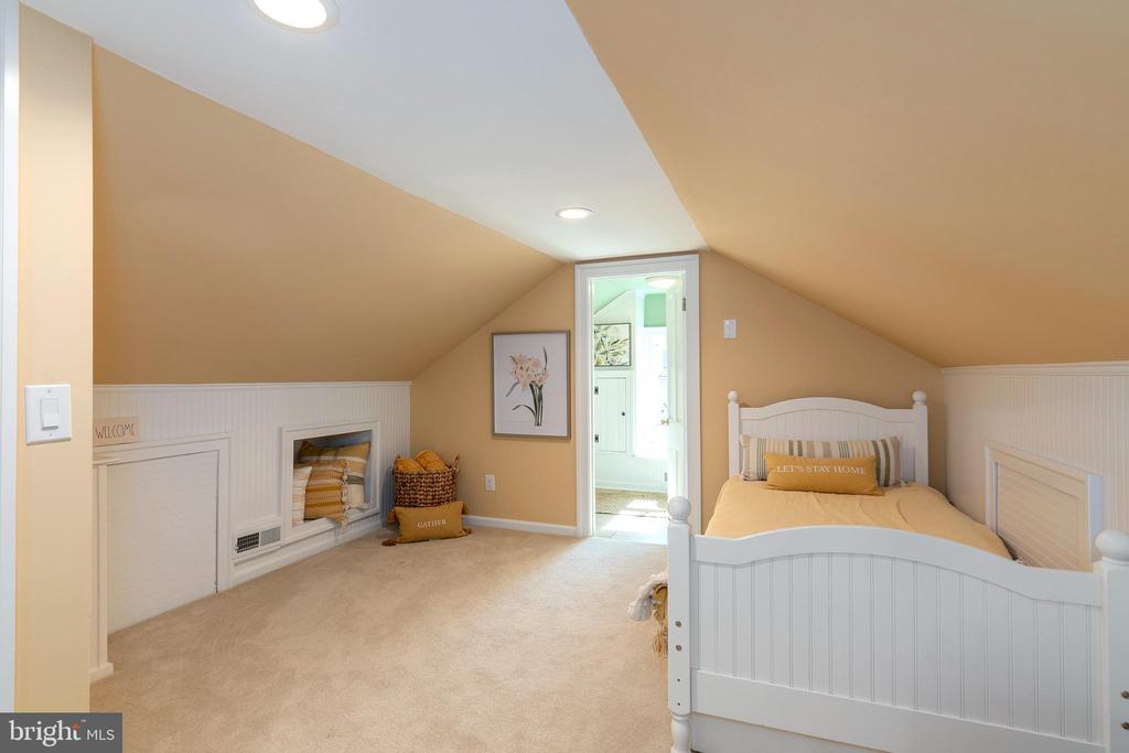 Attic bedroom with sloped ceilings, white bed, beige carpet, and bright adjoining room.