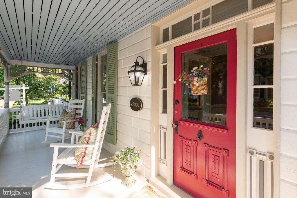 Covered front porch with white rocking chairs and green shutters beside a bright red entrance door.