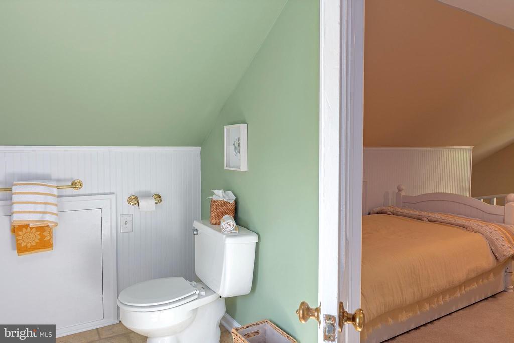 Bathroom with mint-green walls and white toilet, opening into a bedroom with peach bedding.