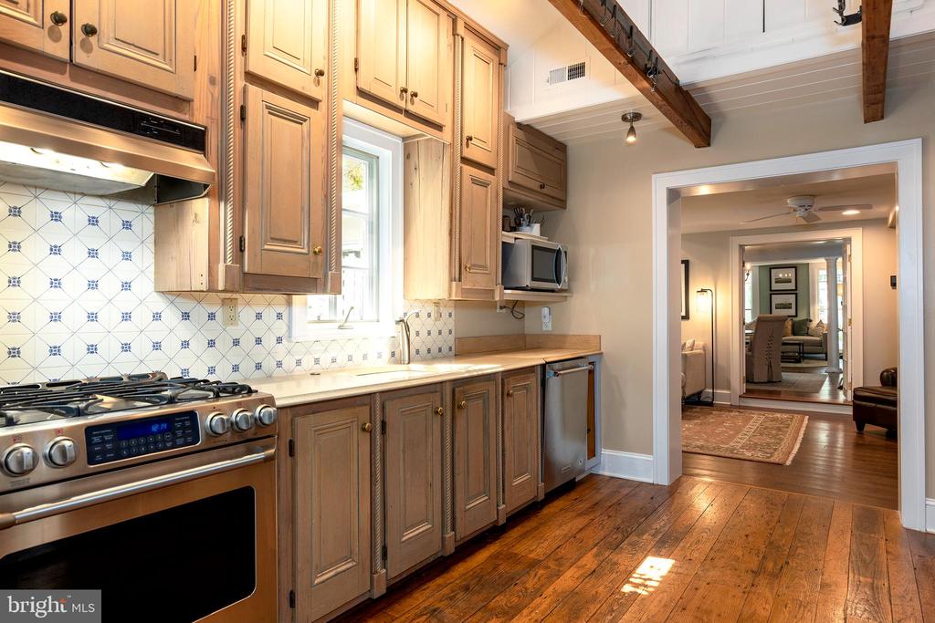 Kitchen with warm wood cabinetry, patterned tile backsplash, stainless steel gas range, and hardwood floors.