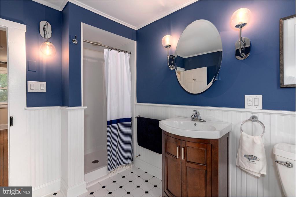 Bathroom with navy walls, a wood vanity, round mirror, and striped shower curtain.