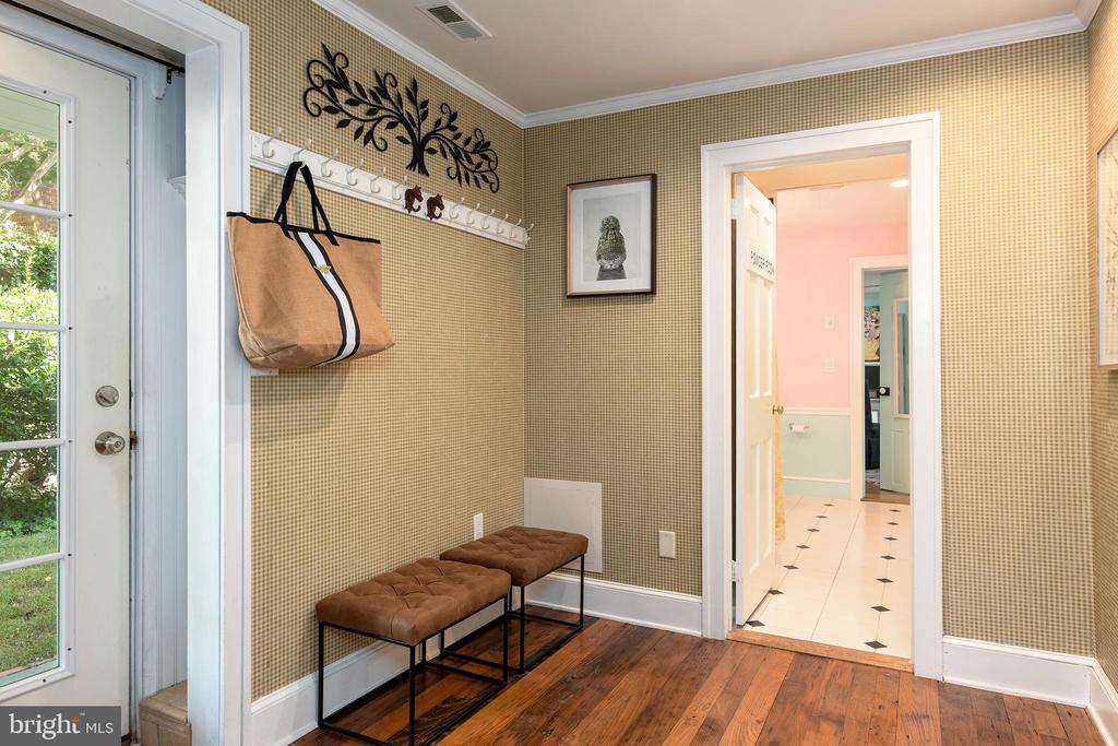 Entryway with patterned wallpaper, coat hooks, two brown benches, and hardwood flooring.