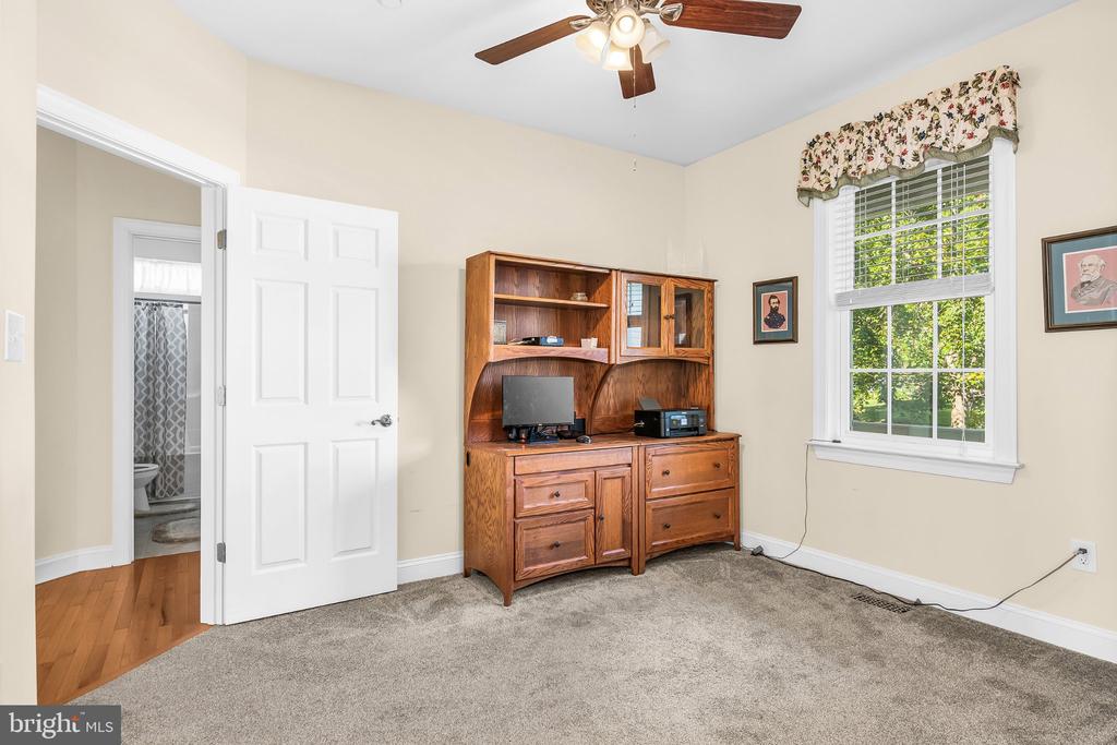 Furnished carpeted room with a wooden entertainment cabinet, ceiling fan, and large window.