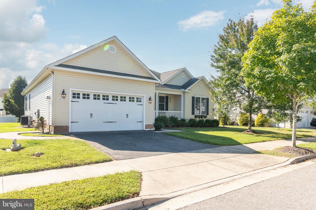 Single-story house with an attached two-car garage, covered porch, and mature trees.