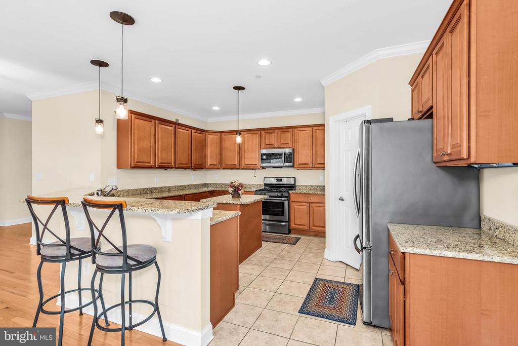 Kitchen with warm wood cabinets, granite countertops, and a breakfast bar with two stools.