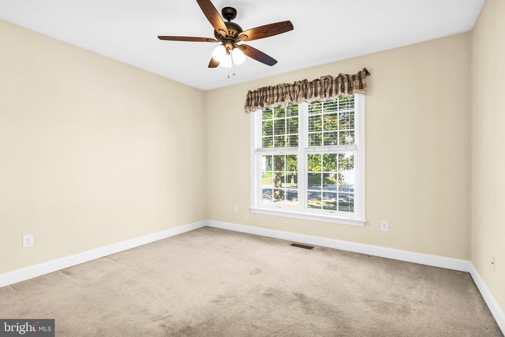 Empty carpeted room with beige walls, a large window, and a dark wood ceiling fan.