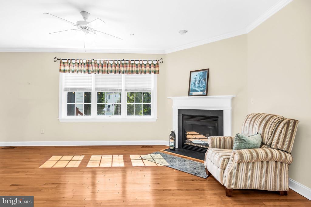 Living room with hardwood floors, a white fireplace, broad windows, and a striped armchair.