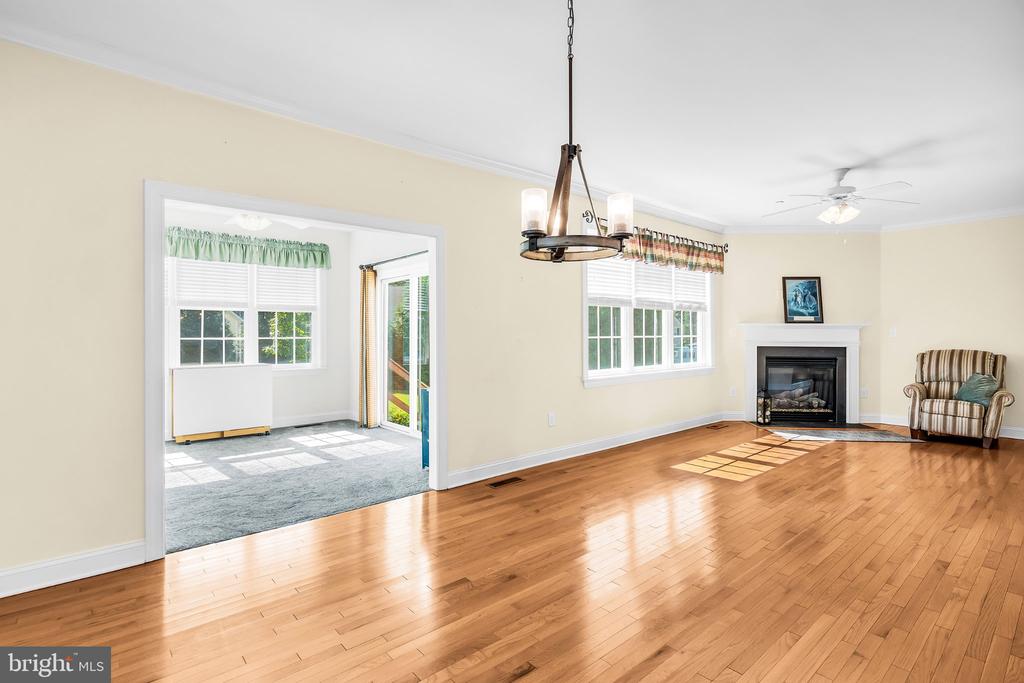 Living room with hardwood floors, a fireplace, and a wide doorway to a sunny adjoining room.