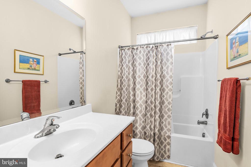 Bathroom with a wood vanity, white tub-shower, patterned curtain, and red towels.