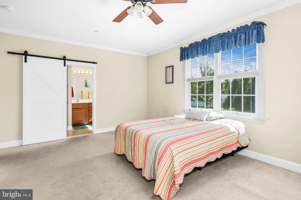Bedroom with a striped bedspread, blue window curtains, and a sliding barn door to the bathroom.