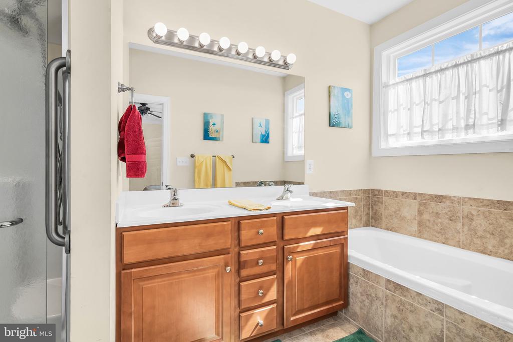 Bathroom with a double-sink wood vanity, tiled bathtub surround, and separate glass-enclosed shower.