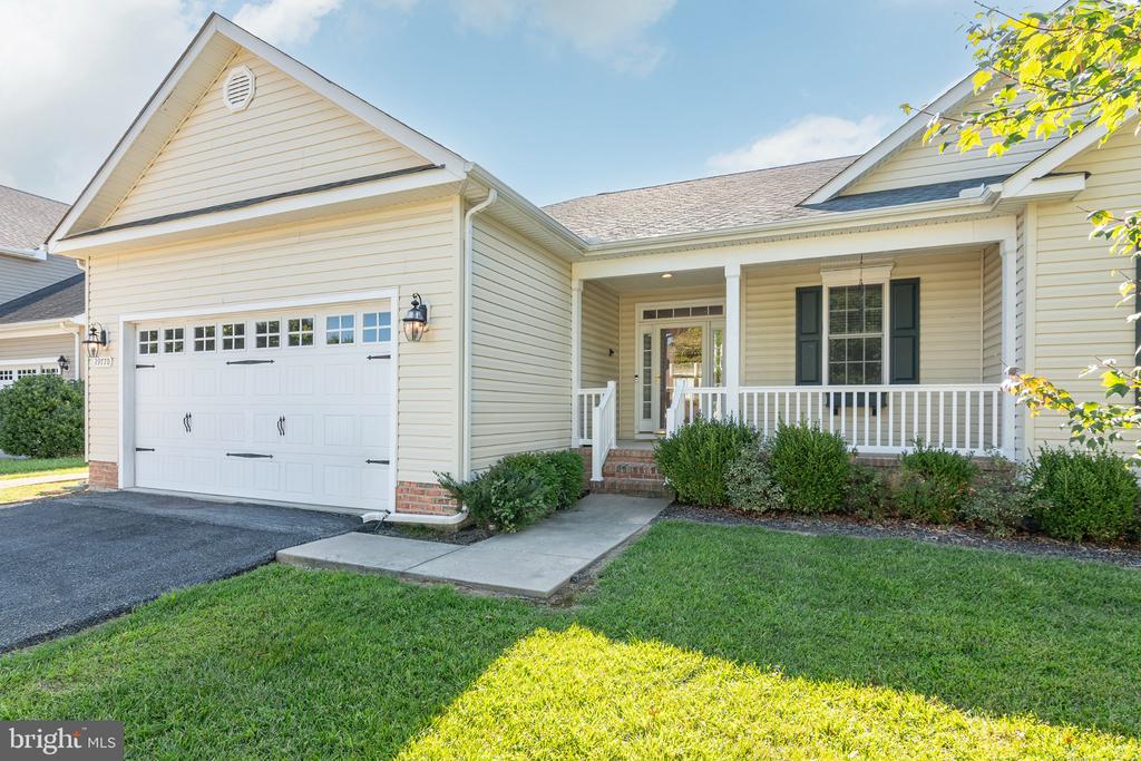 Beige single-story home with a white garage door, covered porch, and green lawn.