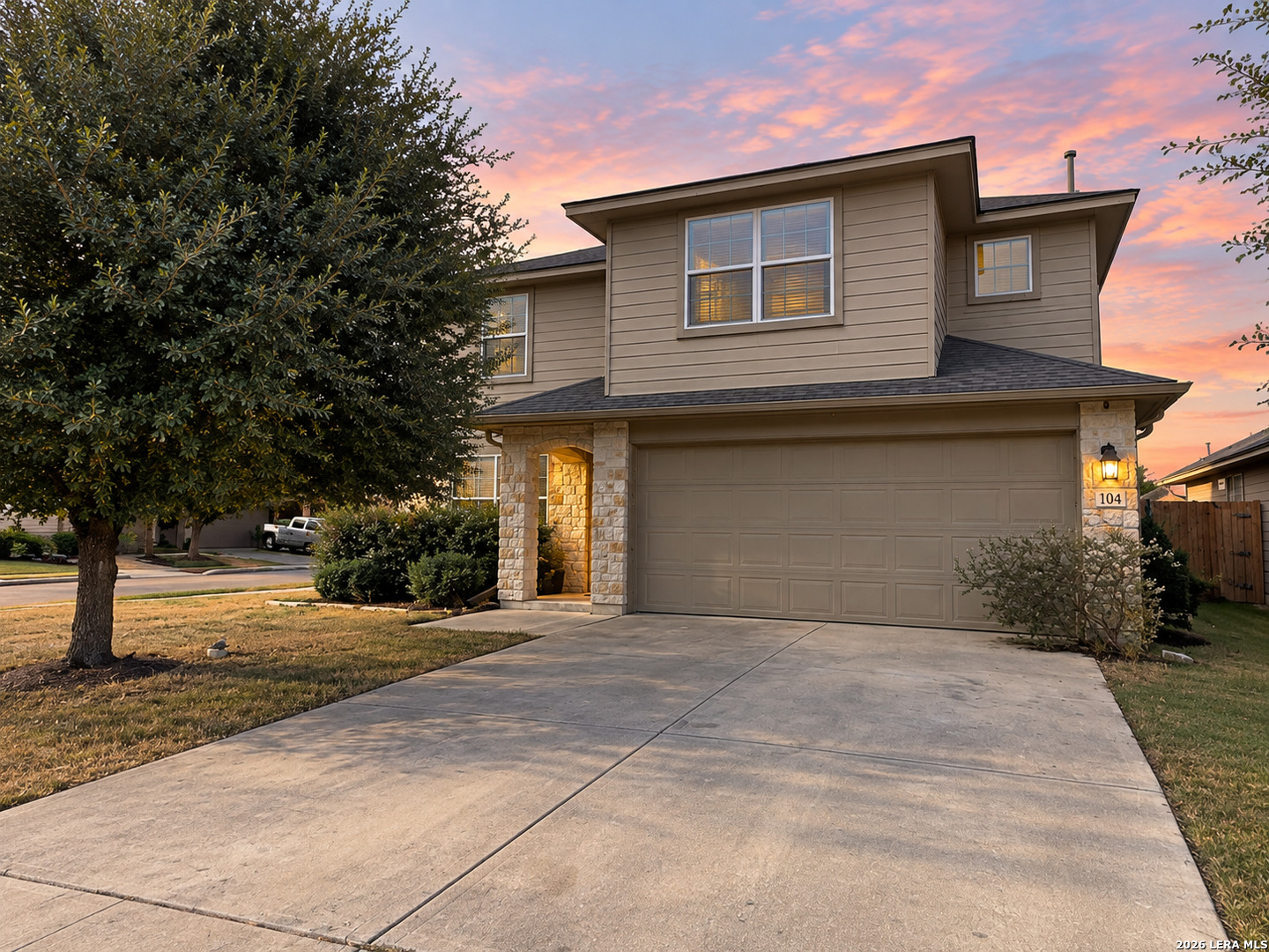 Two-story beige house with a stone entry and double garage beneath a pink dusk sky.