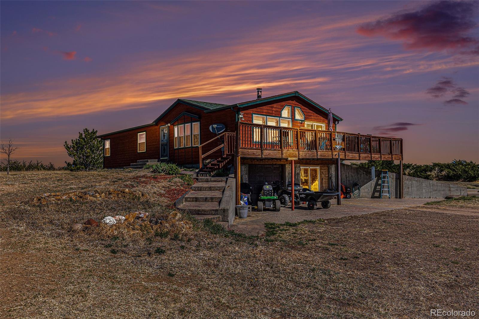 Wood-sided home with a raised deck and garage beneath a colorful sunset sky.