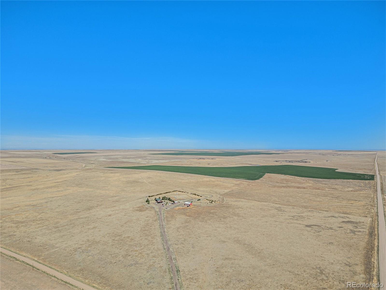 Aerial view of rural acreage with a small building cluster, green fields, and dirt roads.